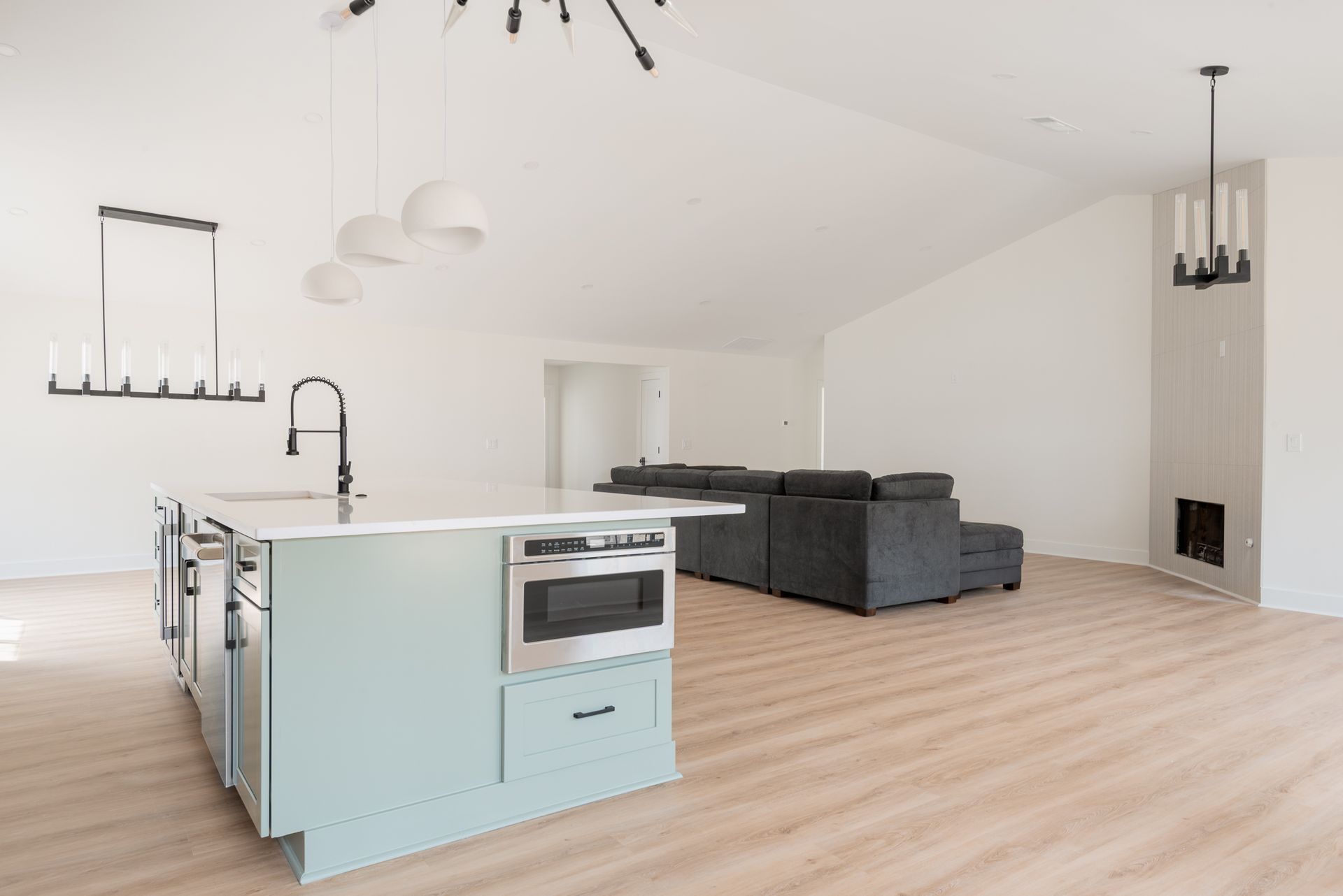 Bright open-plan kitchen and living room with white walls, light wood floors, and dark gray sectional sofa