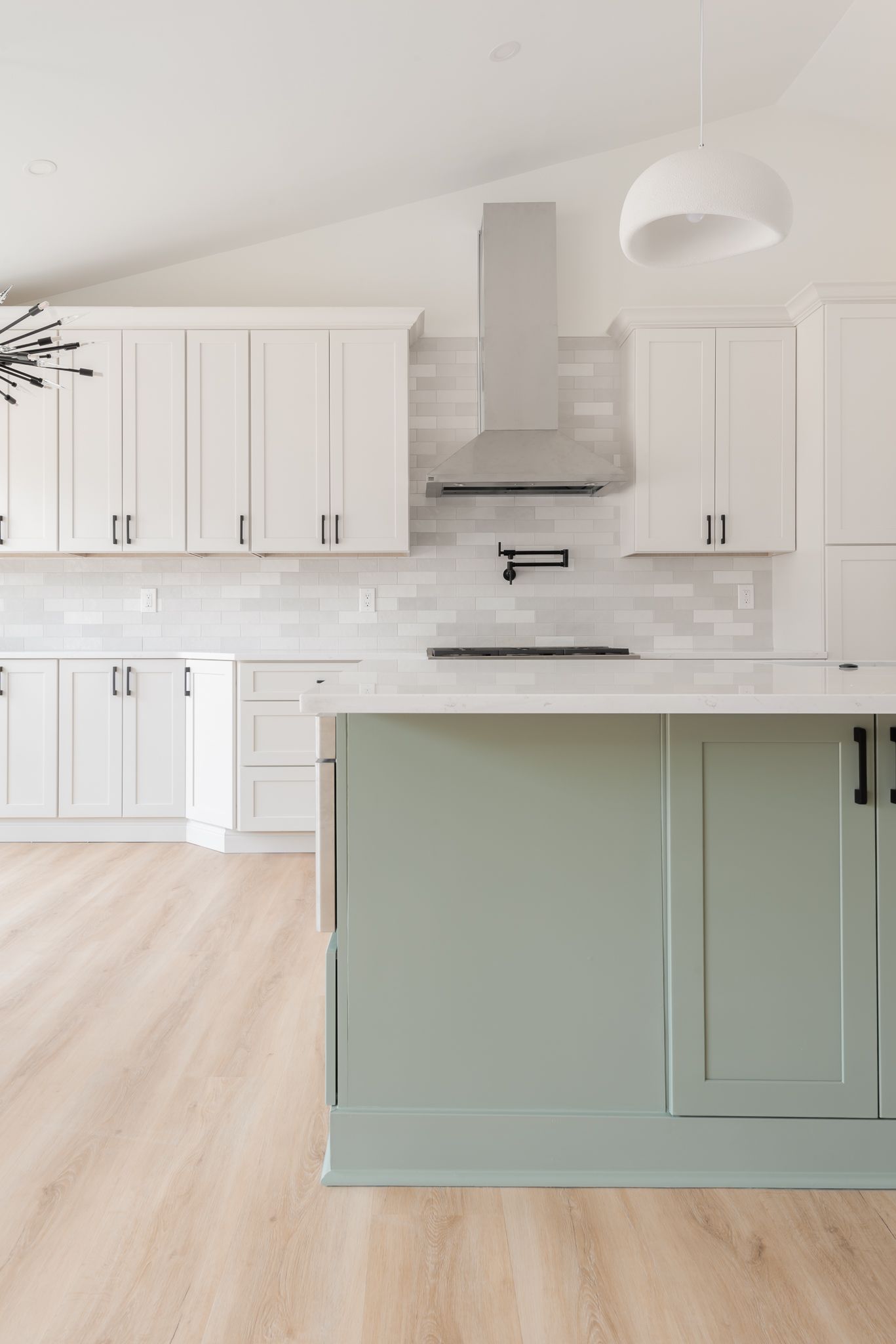 Bright modern kitchen with white cabinets, marble backsplash, and sage-green island