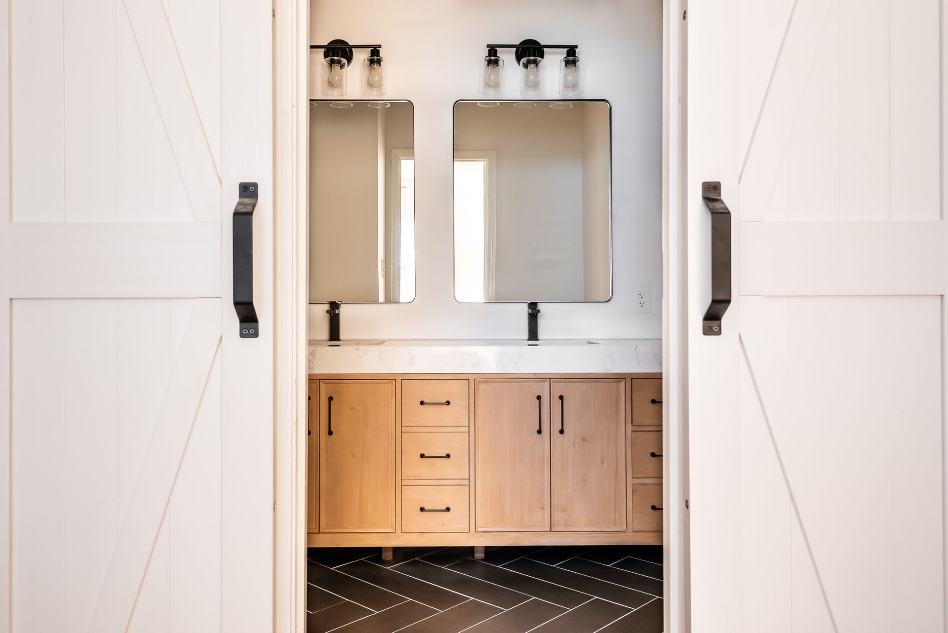 Modern bathroom vanity with twin mirrors, wood cabinets, and white barn doors open on either side