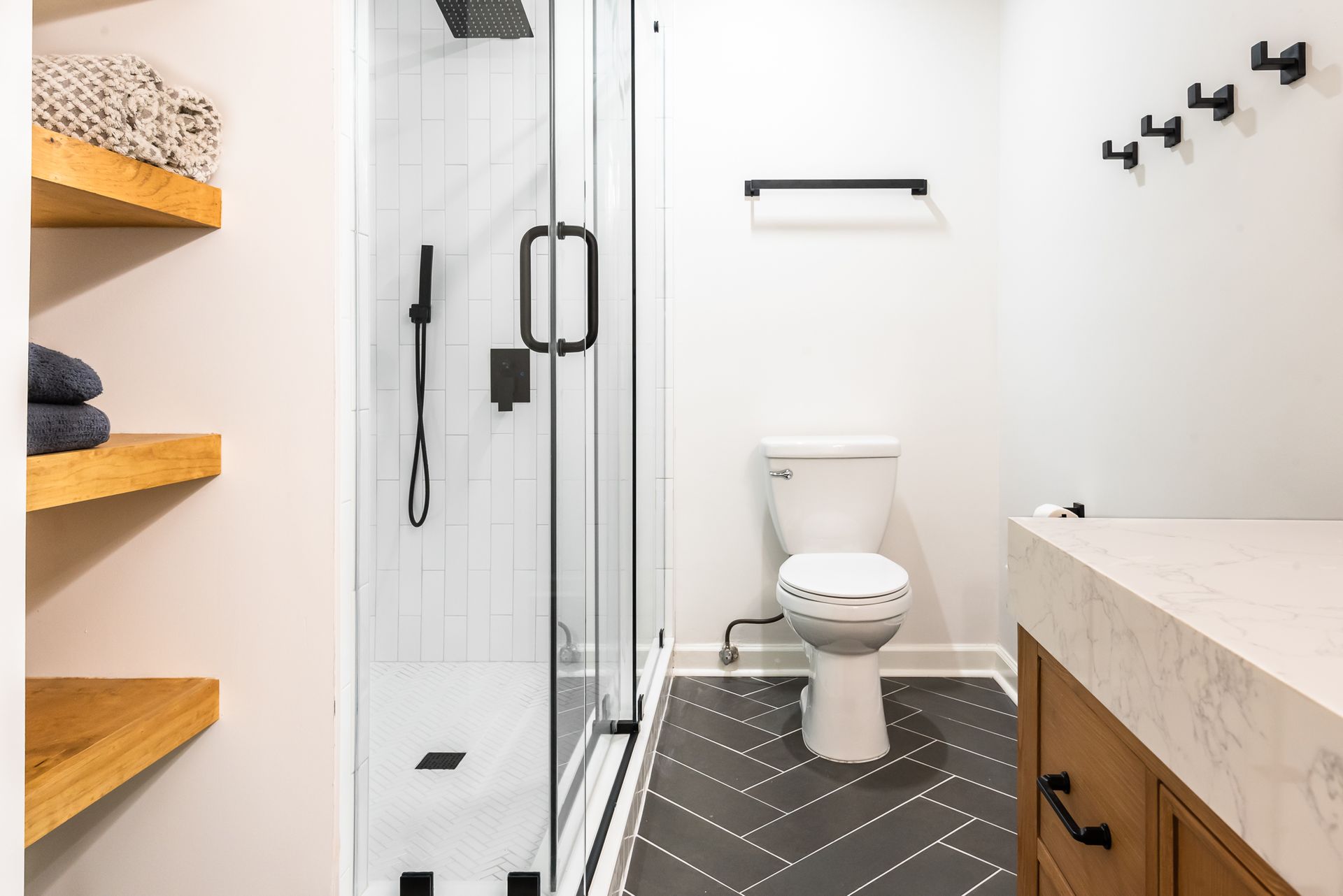 Modern bathroom with walk-in shower, toilet, and white walls with black accents.