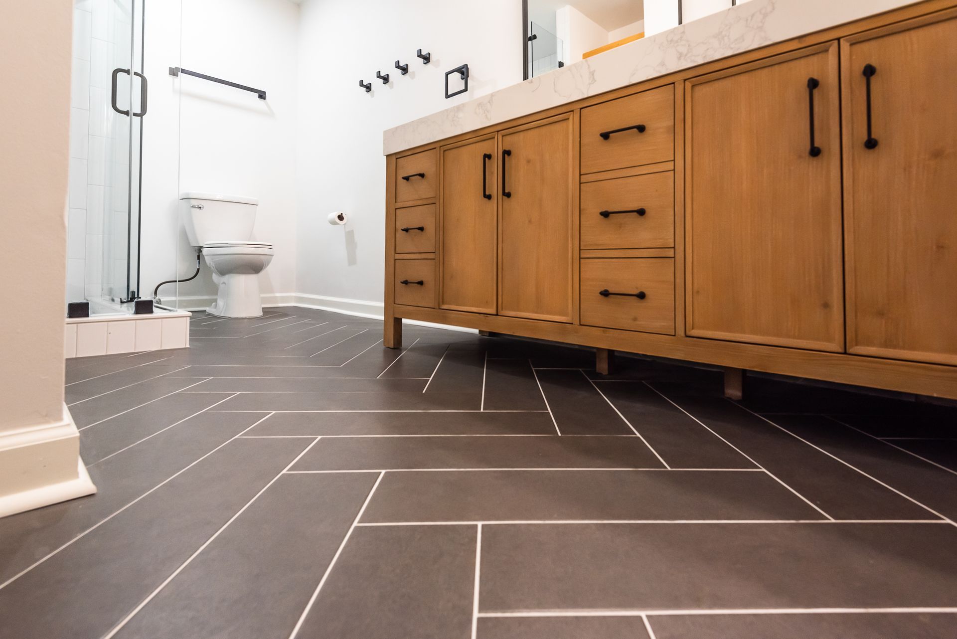 Modern bathroom with wood vanity, white walls, and dark floor tiles
