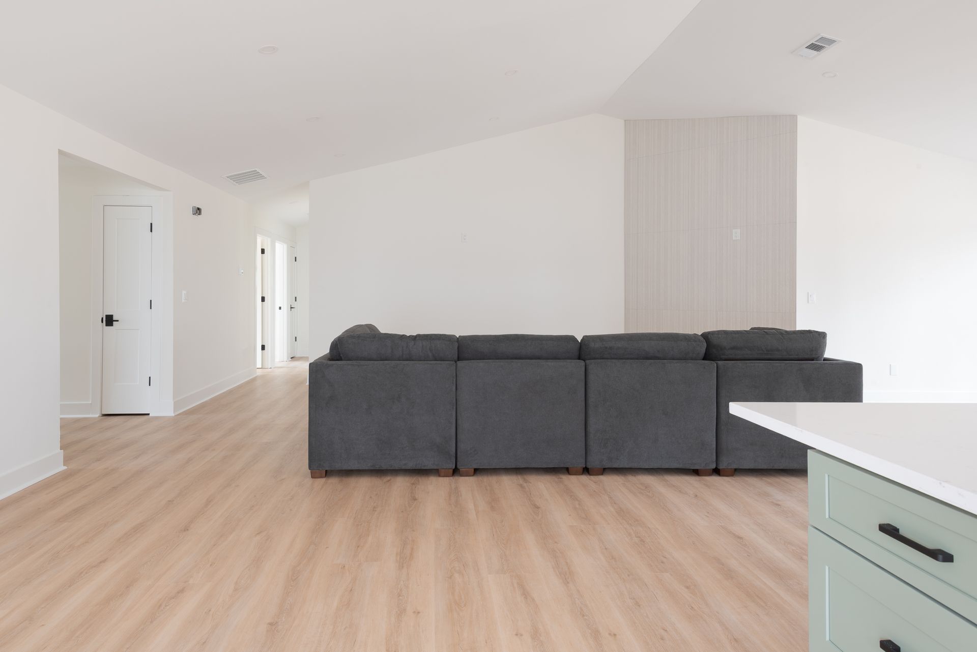 Bright empty living room with light wood floors, gray sectional sofa, and white walls
