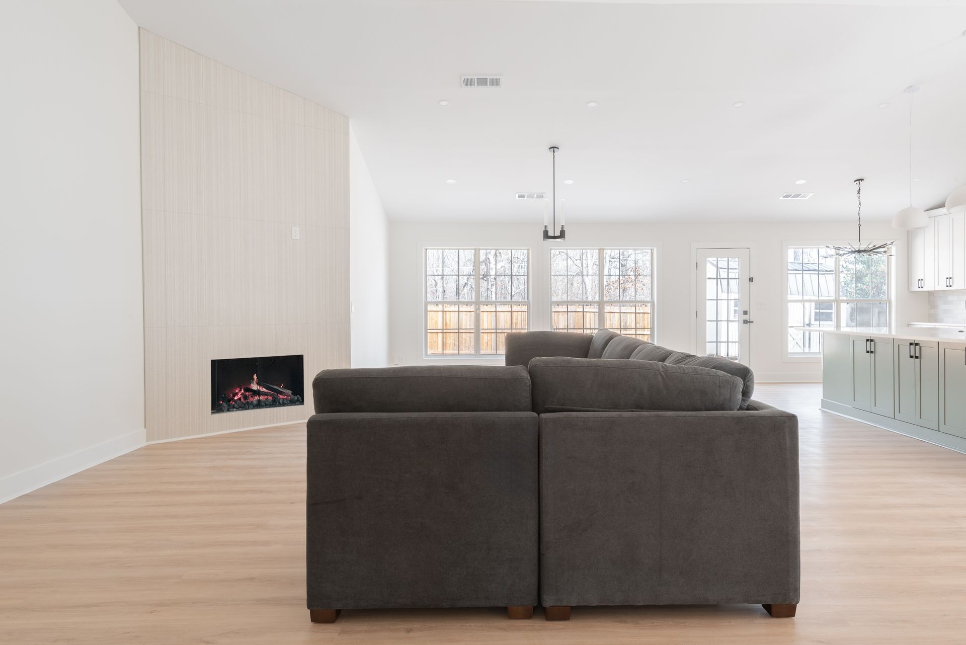 Bright modern living room with dark sectional sofa, fireplace, and open kitchen in the background