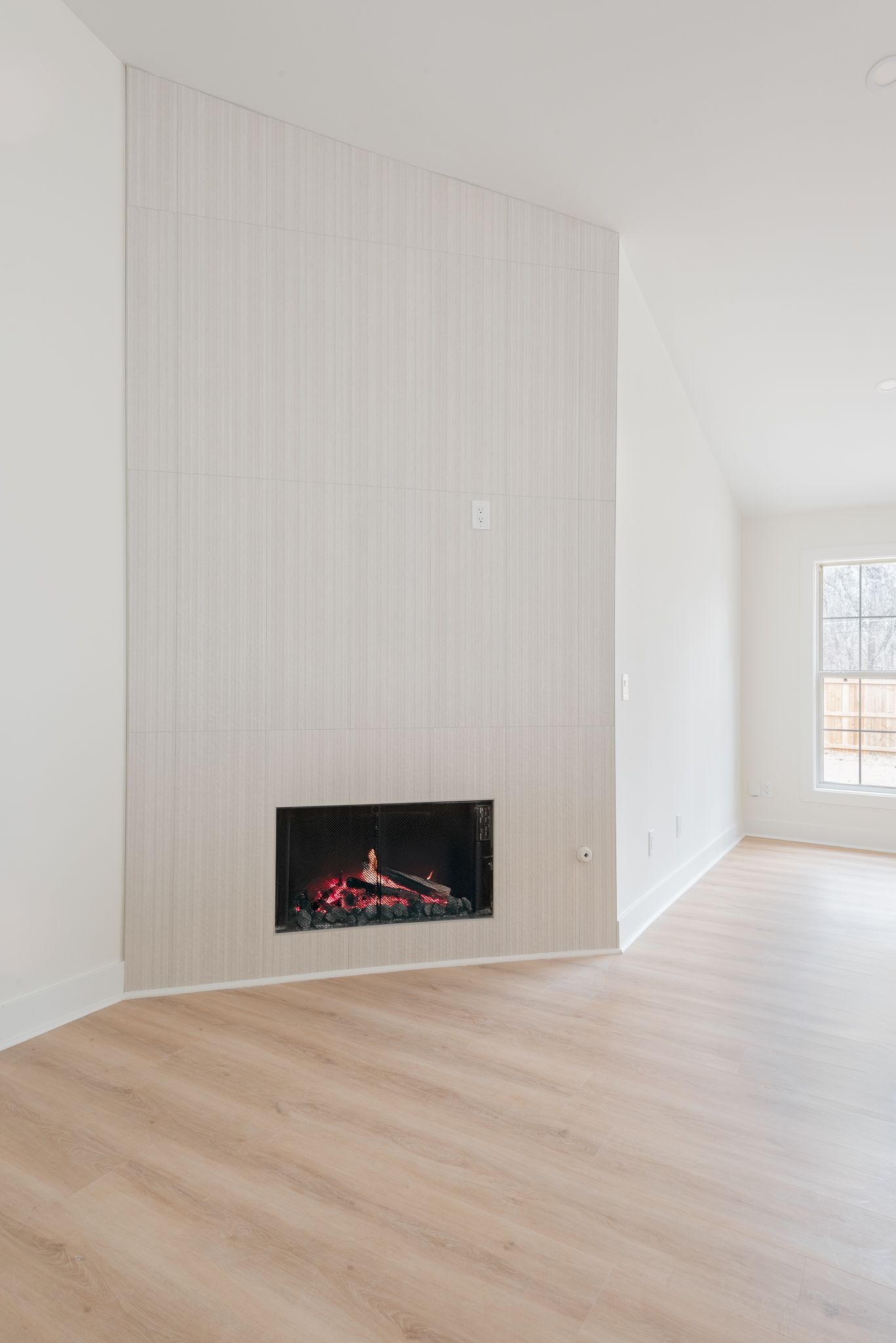 Bright modern room with white walls, light wood floors, and a black wall fireplace on a tiled accent wall.