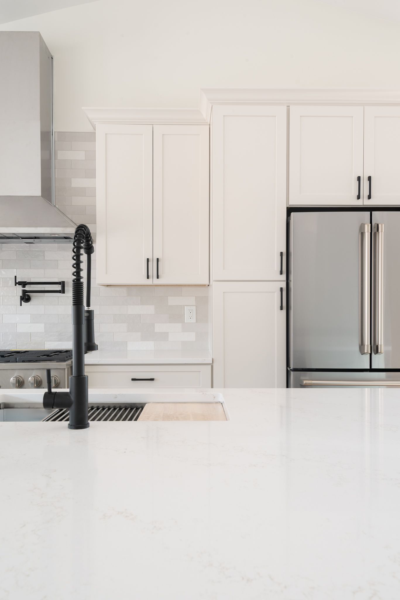 Modern white kitchen with stainless steel refrigerator and marble countertops
