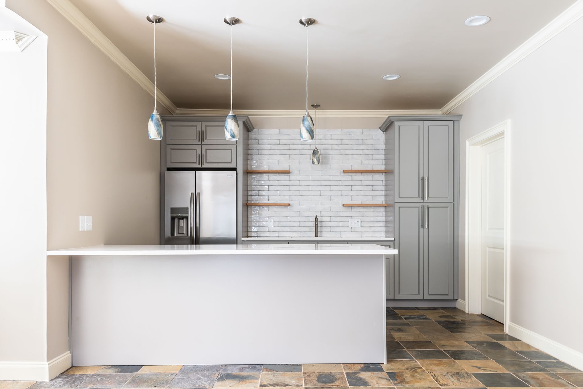 Empty modern kitchen with white island, gray cabinets, subway tile backsplash, and pendant lights