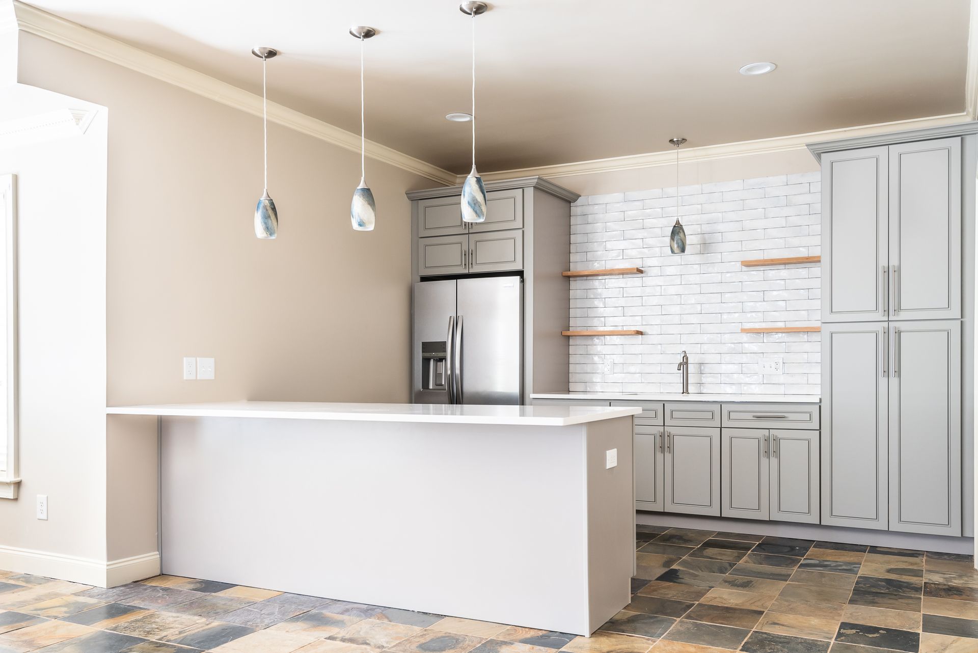 Bright modern kitchen with white island, gray cabinets, pendant lights, and stone tile floor