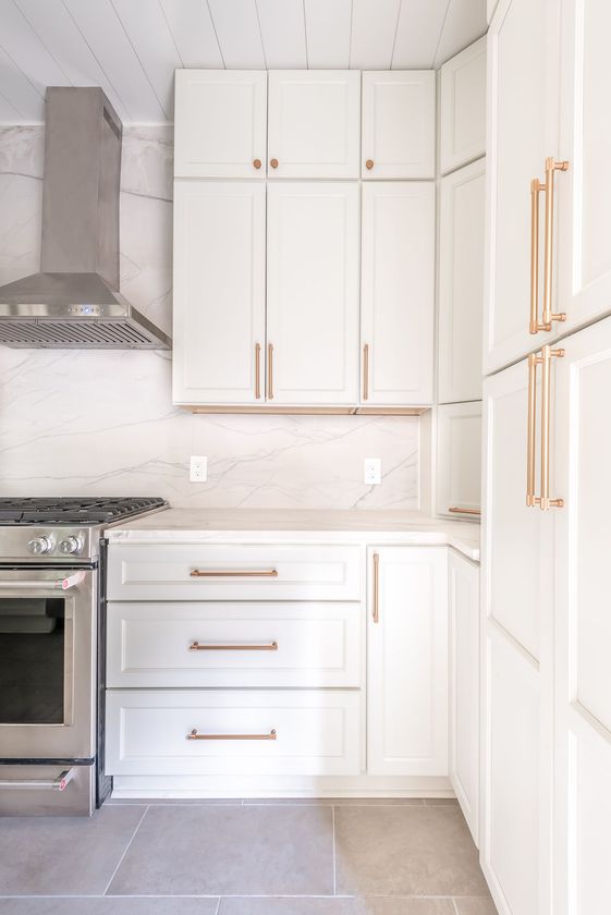Bright white kitchen with stainless steel stove, built-in refrigerator, and gold handles.