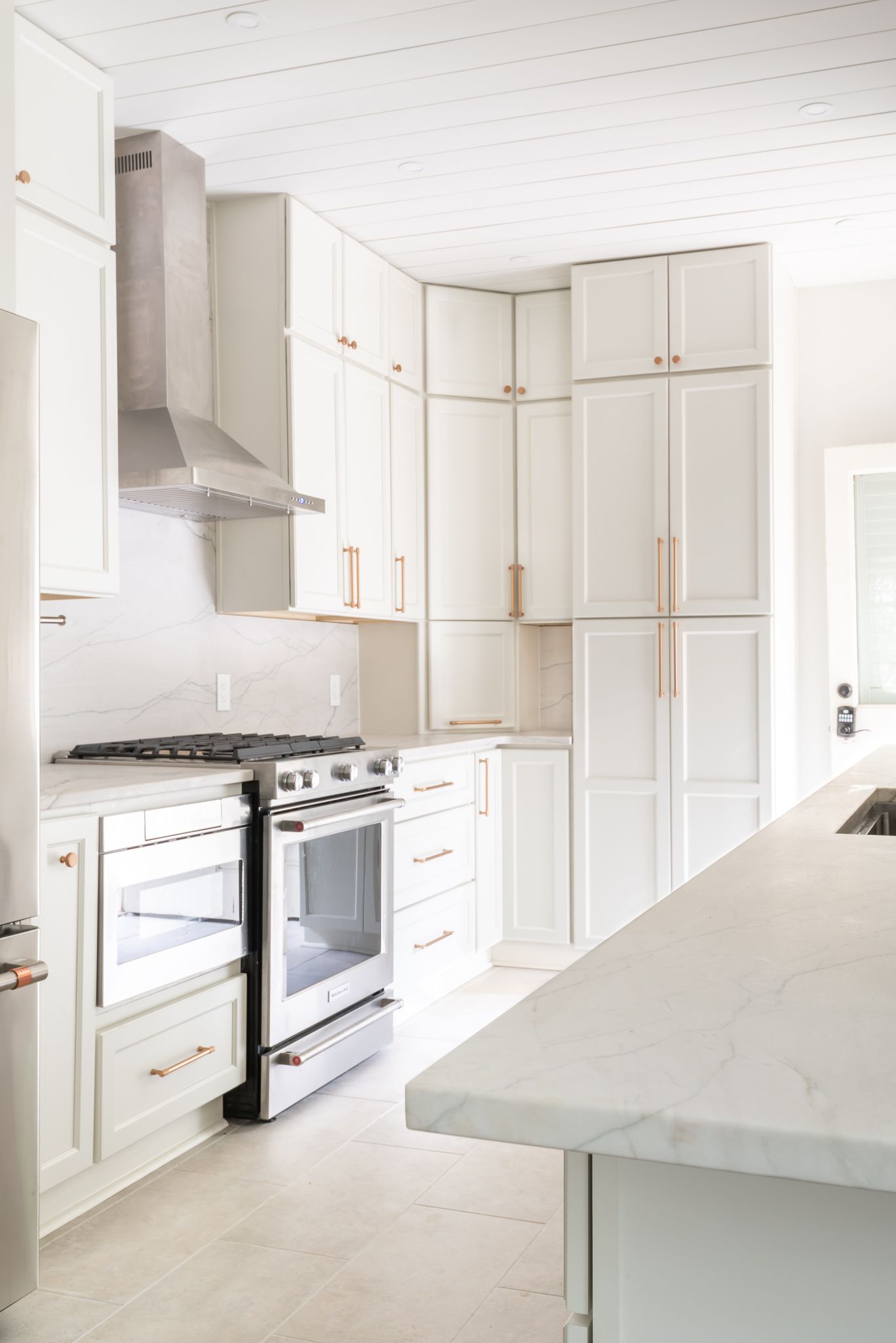 Bright white modern kitchen with tall cabinets, stove, and marble island countertop