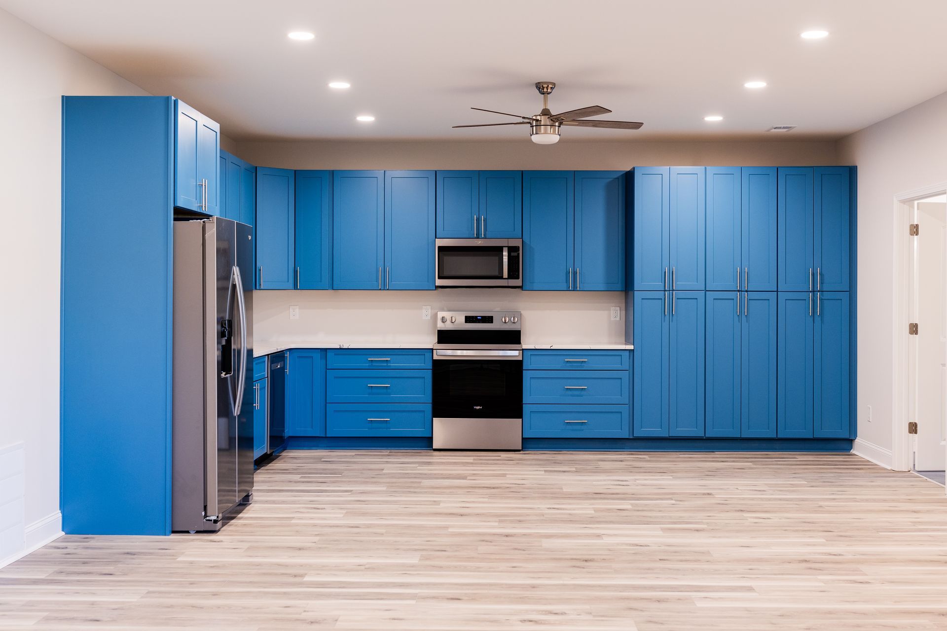 Bright blue kitchen with stainless steel appliances, white backsplash, and light wood flooring