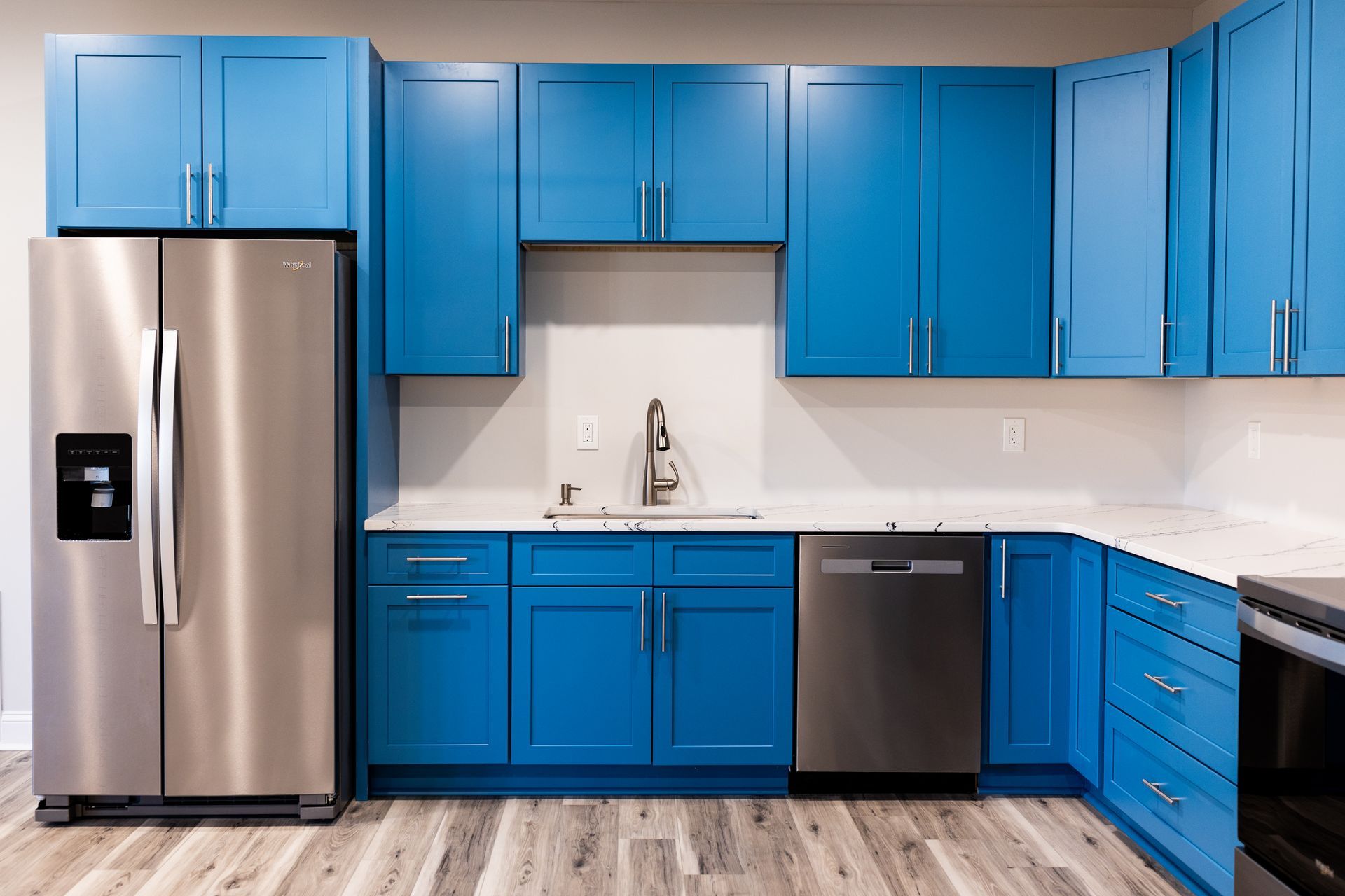 Modern kitchen with bright blue cabinets, stainless steel fridge, and dishwasher on wood flooring