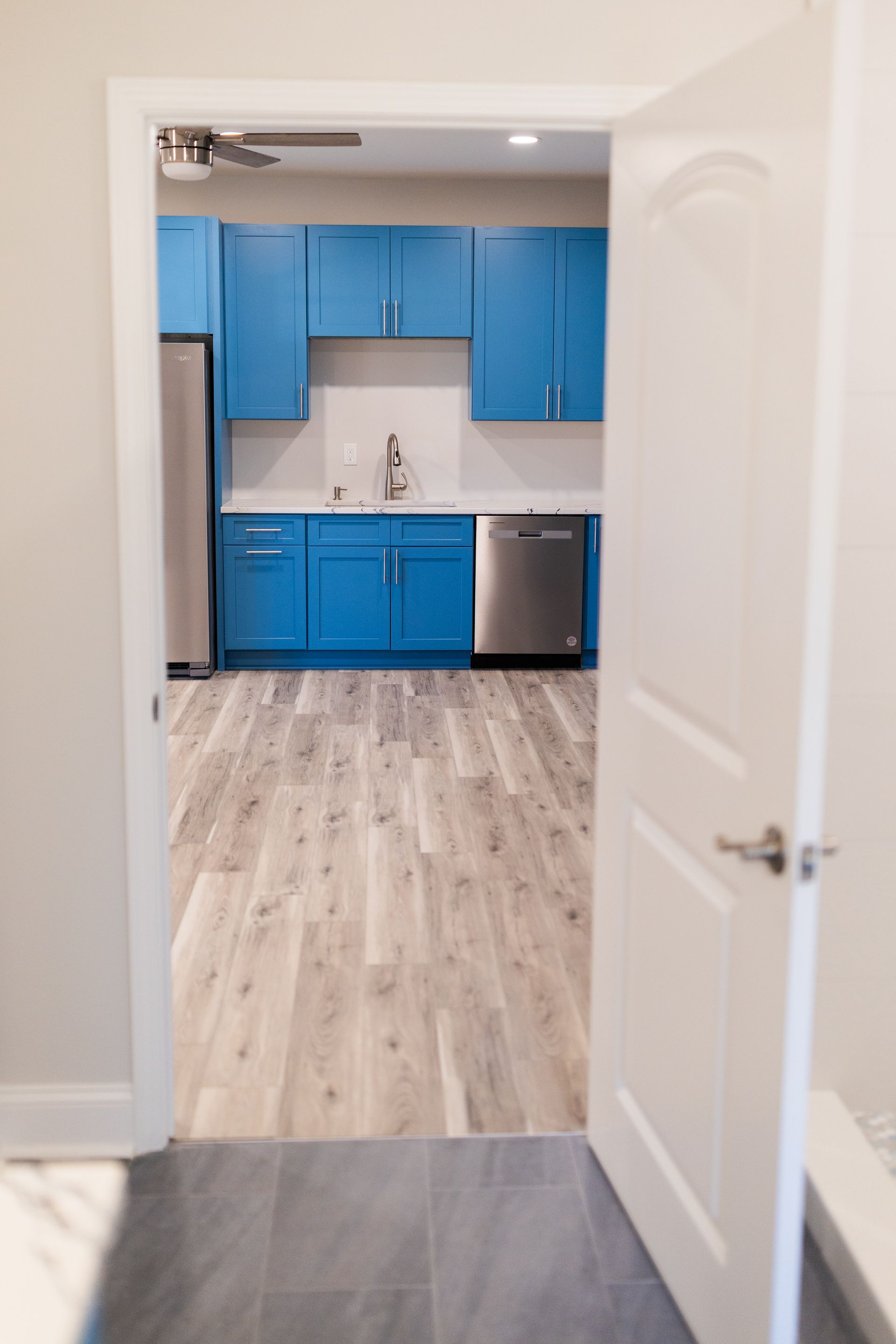 View through a doorway into a small kitchen with bright blue cabinets and light wood flooring.