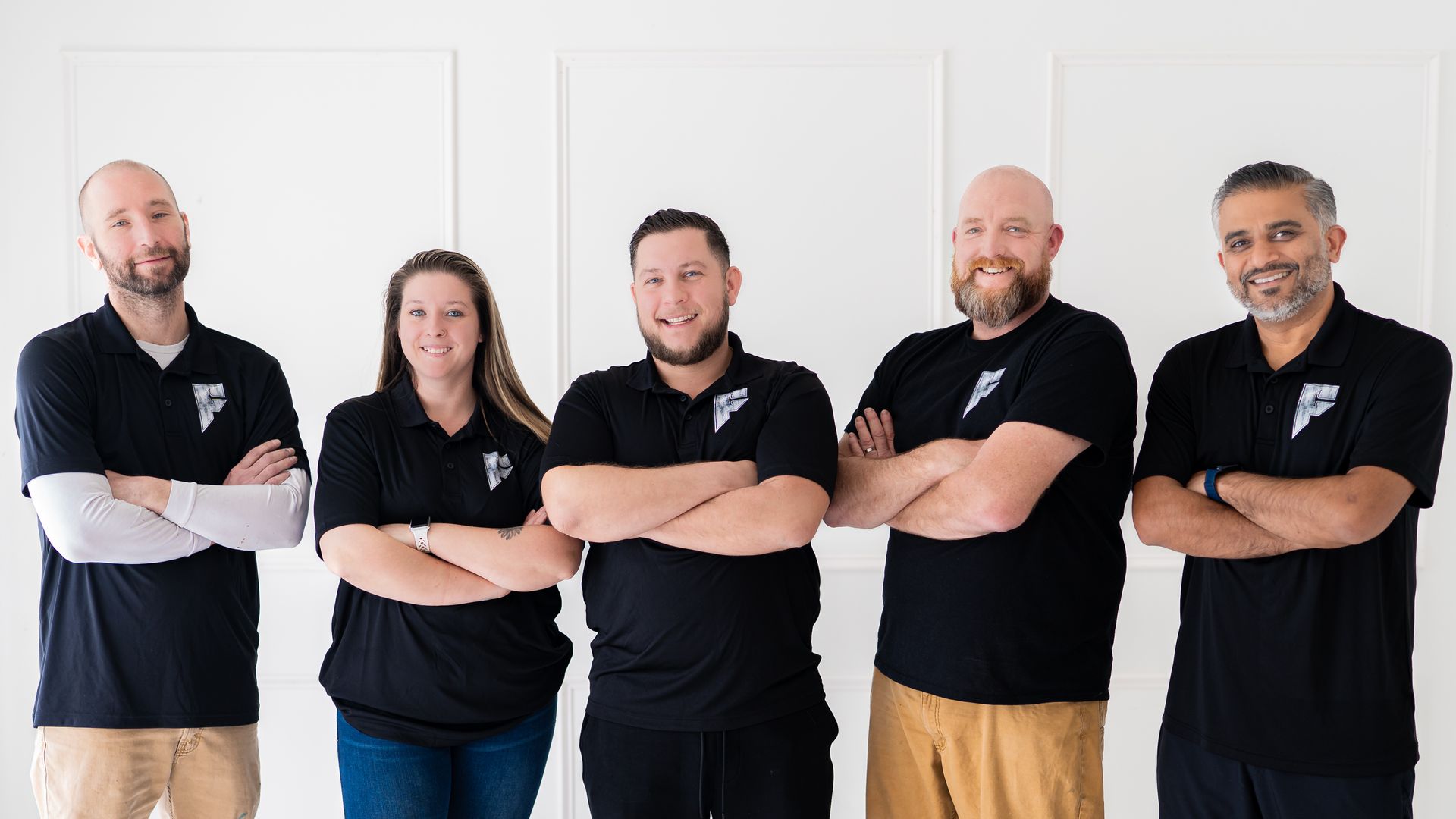 Five team members in black shirts stand with arms crossed against a white wall.