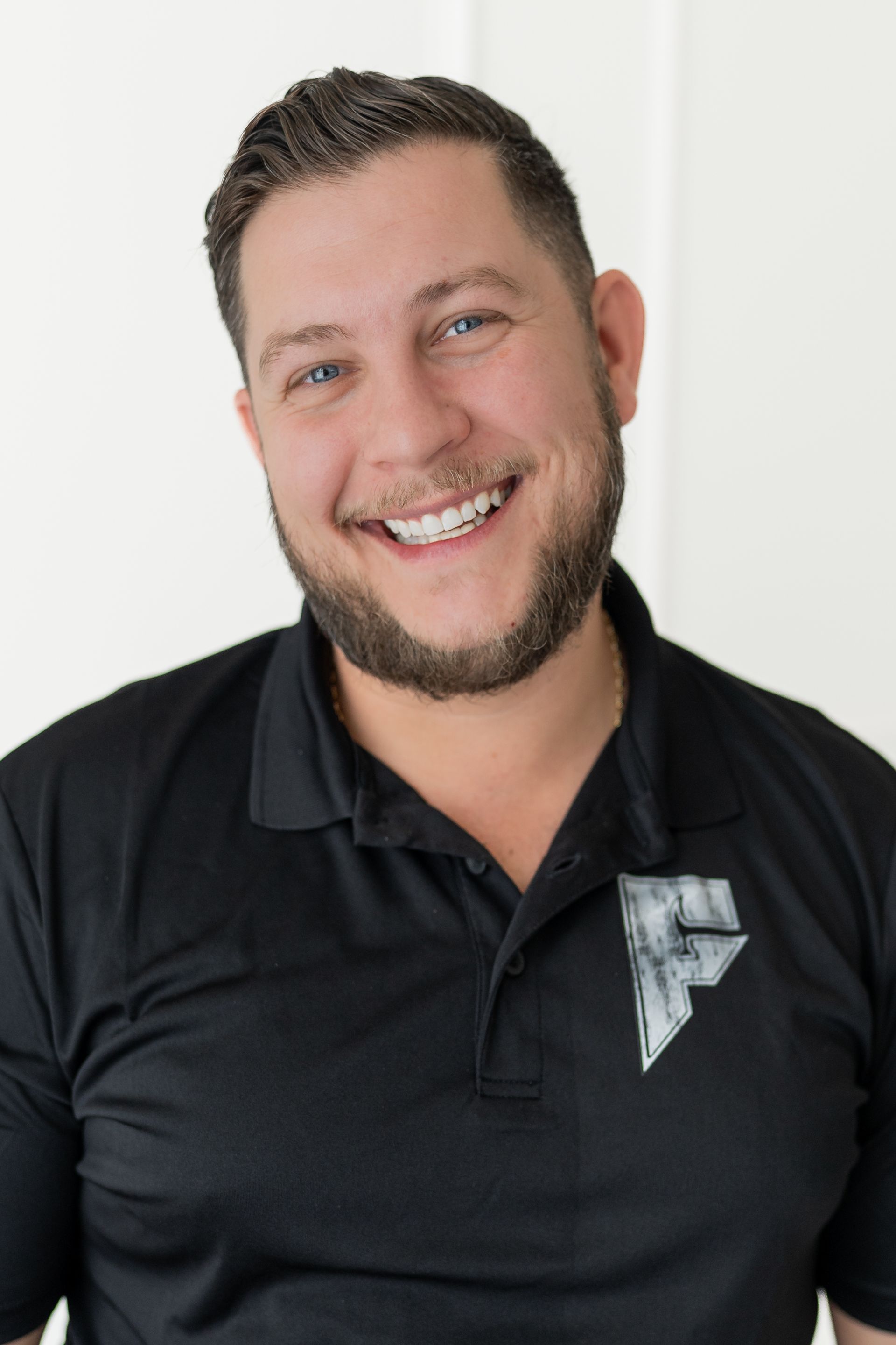 Smiling man in a black polo shirt standing against a light background