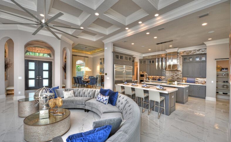 Bright open-plan luxury living room and kitchen with curved gray sofa, blue pillows, and island seating