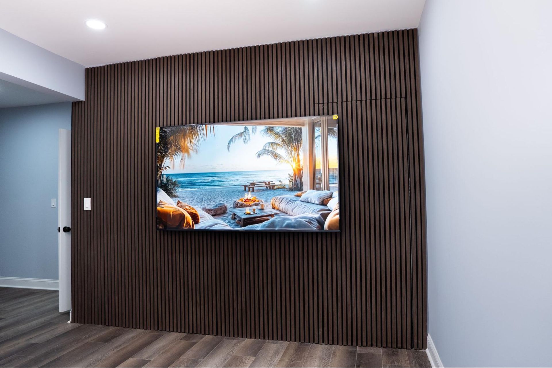 Wall-mounted tropical beach artwork on a dark slatted feature wall in a modern room