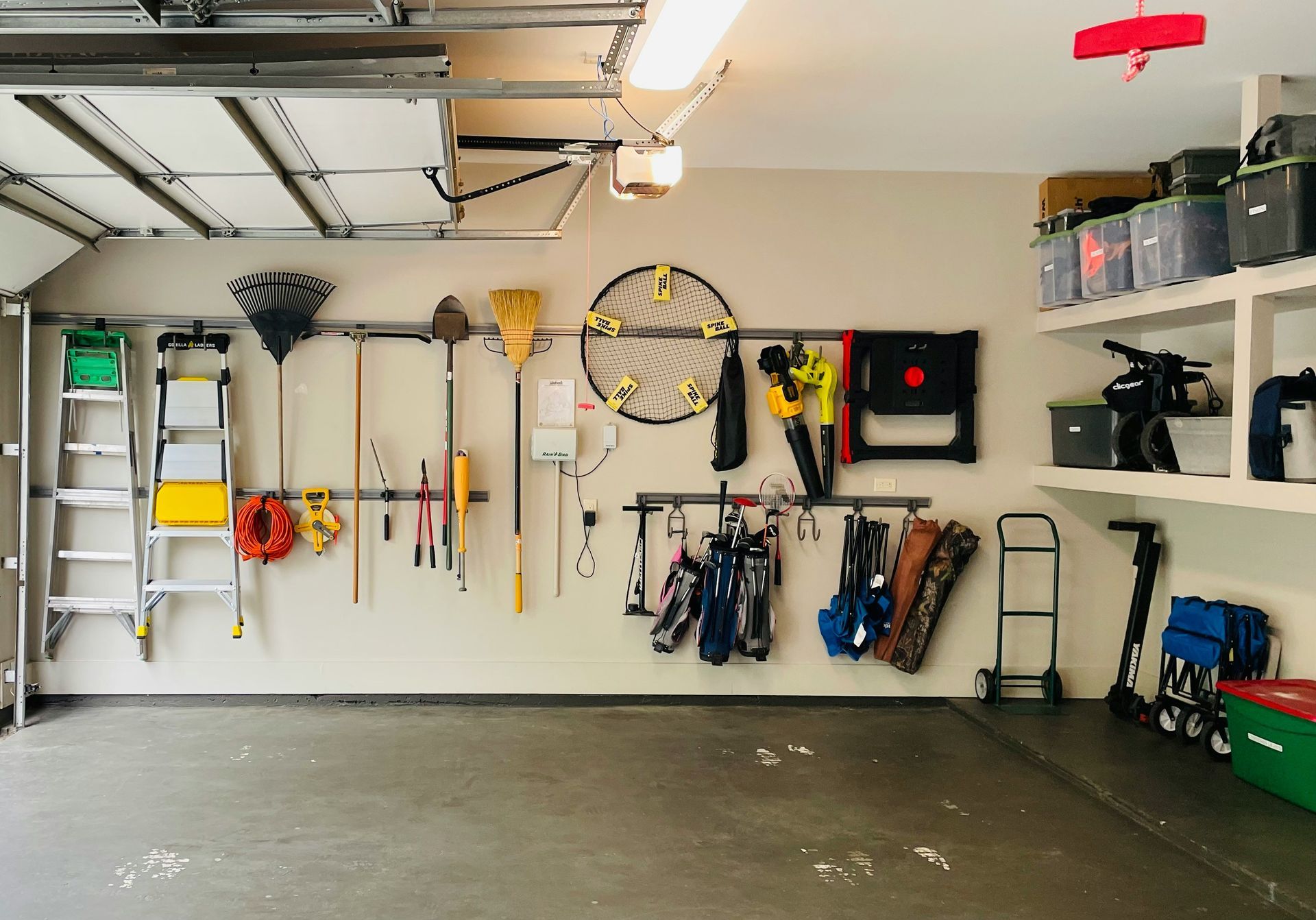 Garage wall with organized tools, ladders, rakes, and sports gear hanging on hooks and shelves.
