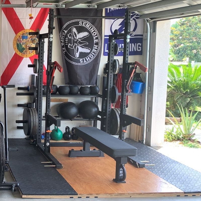 Home gym with a bench, weights, squat rack, stability balls, and a black banner on the wall