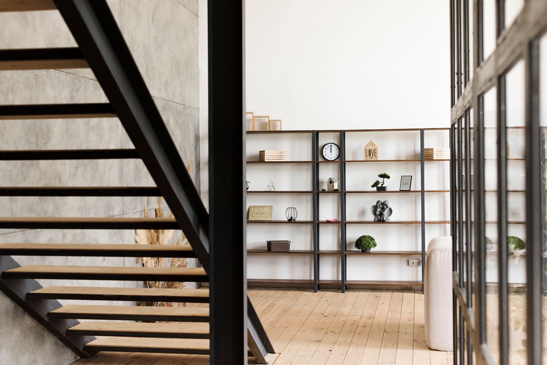 Staircase with black metal railing leads to a room with shelves displaying decor and a large window.