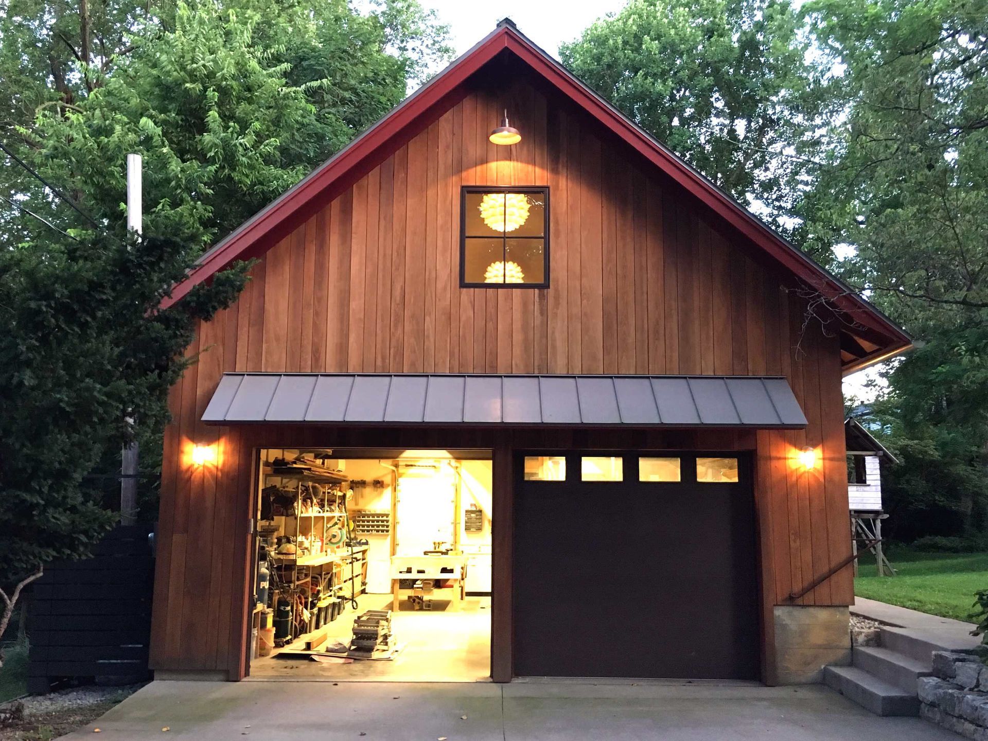 Wooden barn-style garage with a lit open doorway and a closed brown door at dusk
