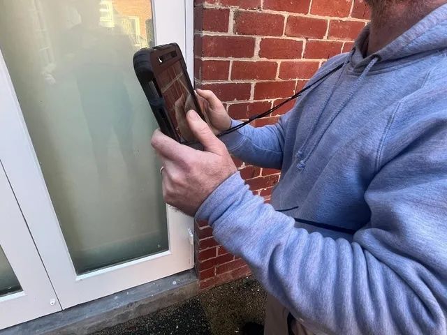 Person in gray sweatshirt using a tablet near a white door, likely taking a photo.