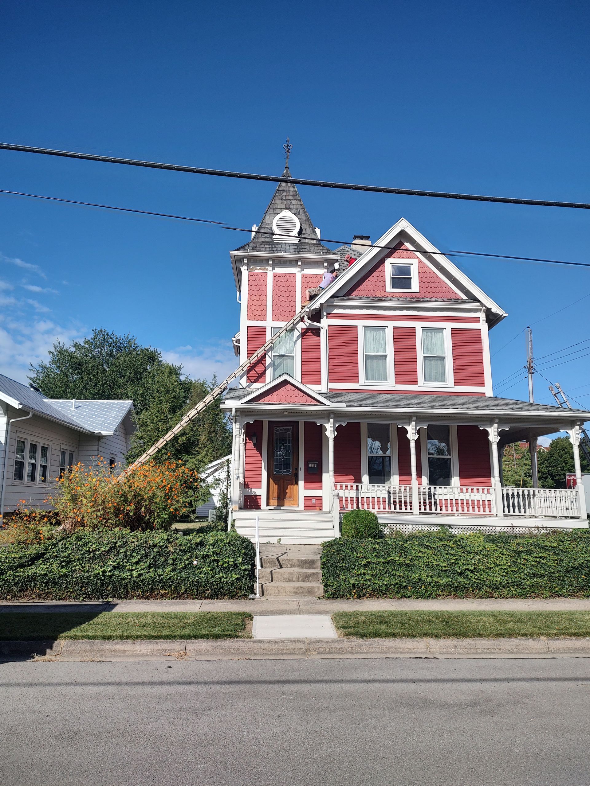 A two-story, red Victorian house with a corner tower and a covered front porch under a clear blue sky.