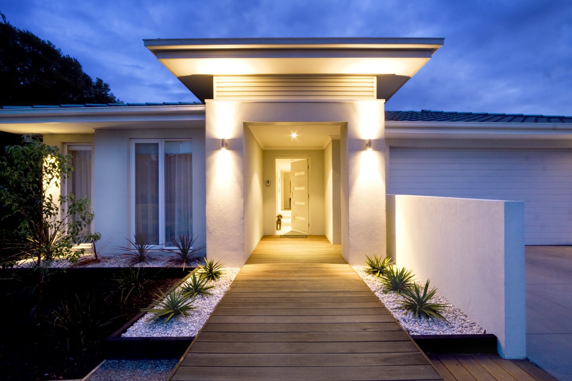 Modern house entrance at dusk with lit pathway and lights.