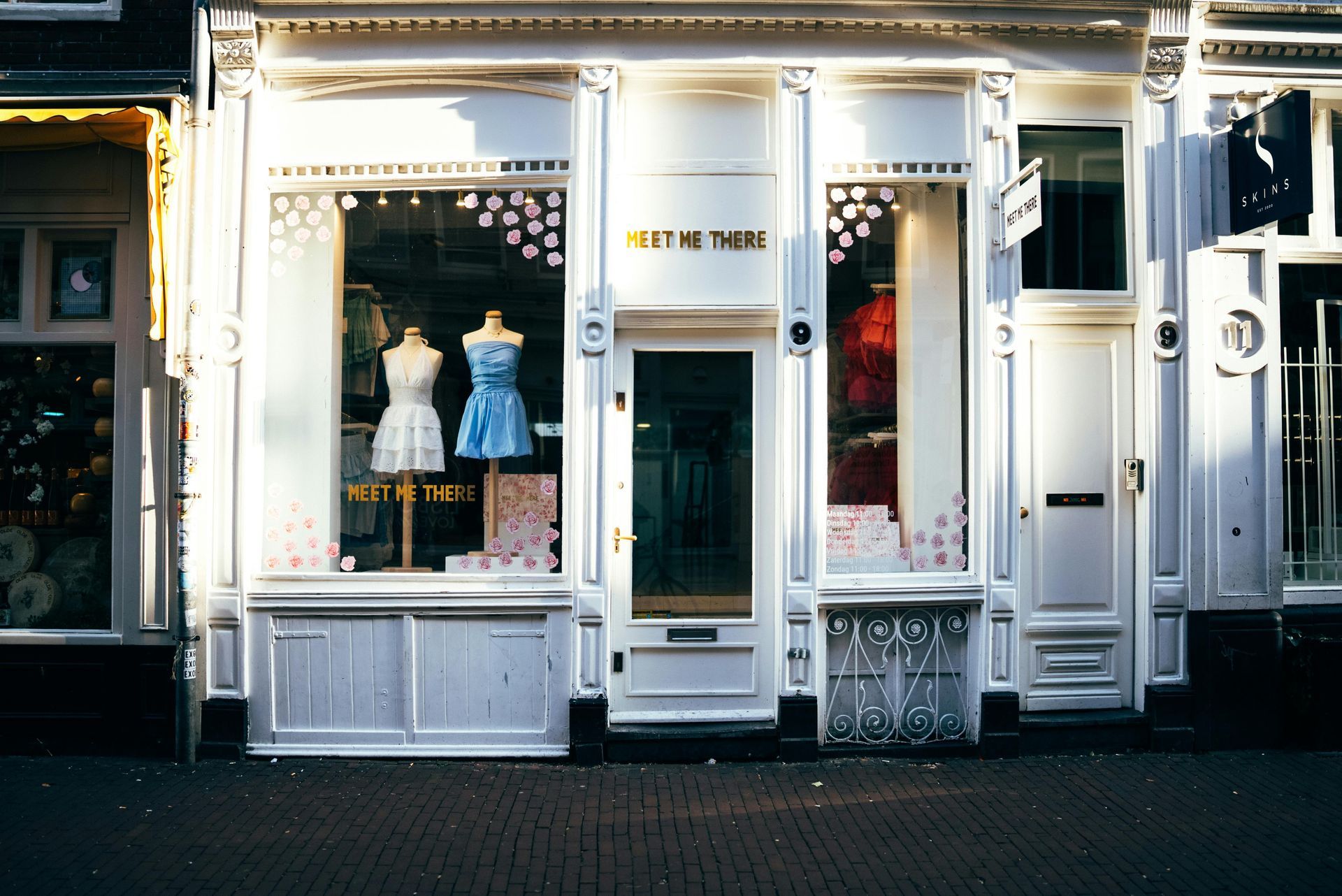 Exterior of a boutique store with white facade, display window mannequins wearing dresses, and the words