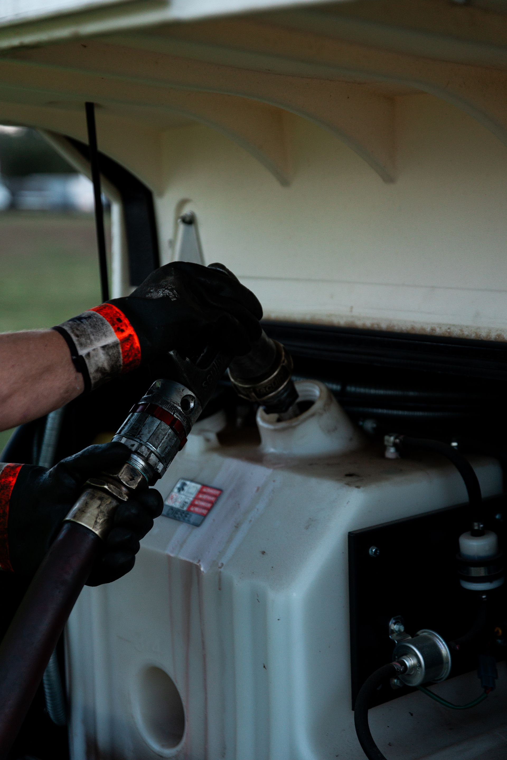 Hands in black gloves refueling a white tank with a hose.
