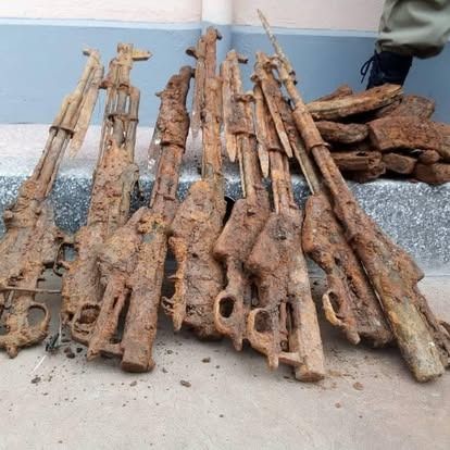 Heavily rusted rifles piled together on a concrete surface, possibly retrieved from water.