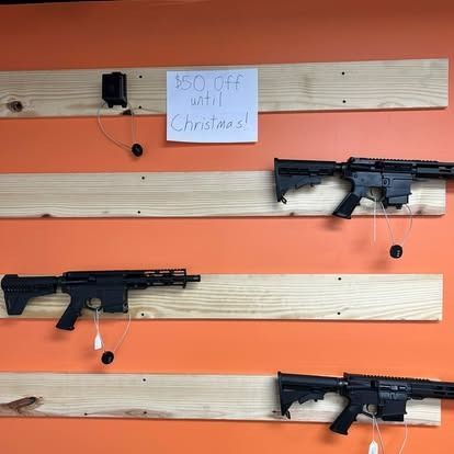 Guns displayed on wooden planks against an orange wall; a sign states 