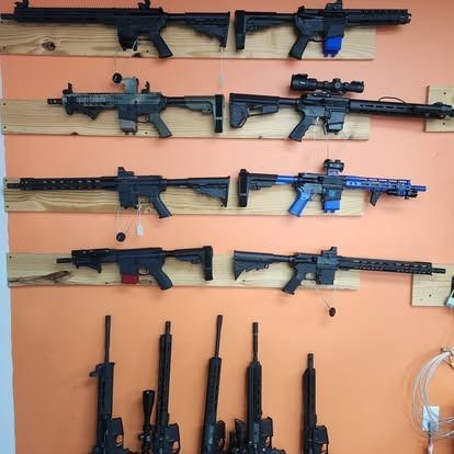 Guns displayed on wooden planks against an orange wall; various models and colors.
