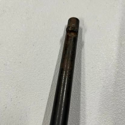 A rusted metal rod against a light-colored surface; the top shows signs of damage.