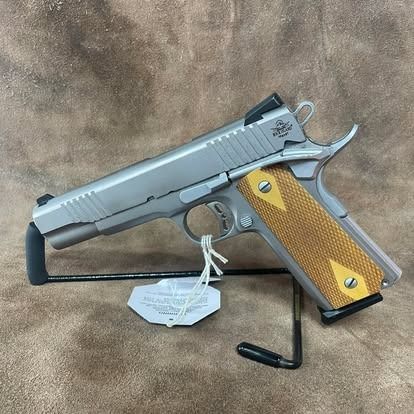 Silver handgun on a black stand, tan grip with yellow diamond accents, set on a brown surface.