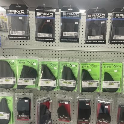 Shelves stocked with various black gun holsters packaged in clear plastic.