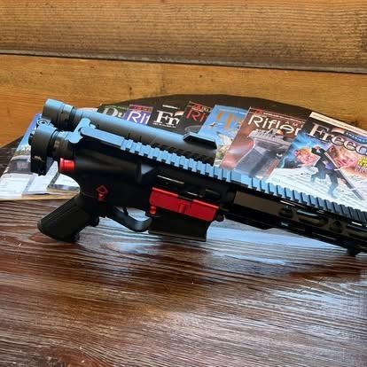 Black and red rifle with a magazine, sitting on top of magazines.