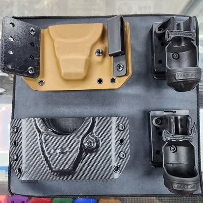 Various gun holsters and magazine carriers mounted on a gray panel, showcasing different styles.