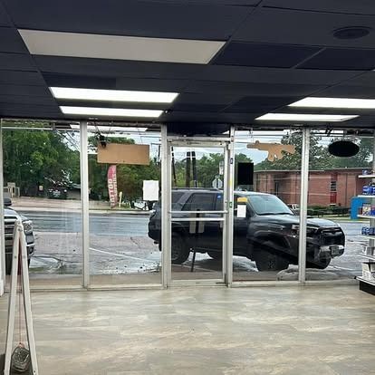 Black SUV parked inside a store. View through glass doors. Reflective wet ground.