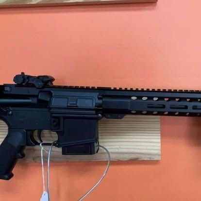 Black AR-15 style rifle on wooden shelf against an orange wall.