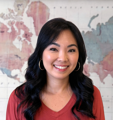 Smiling woman in a red top with hoop earrings, standing before a pastel world map