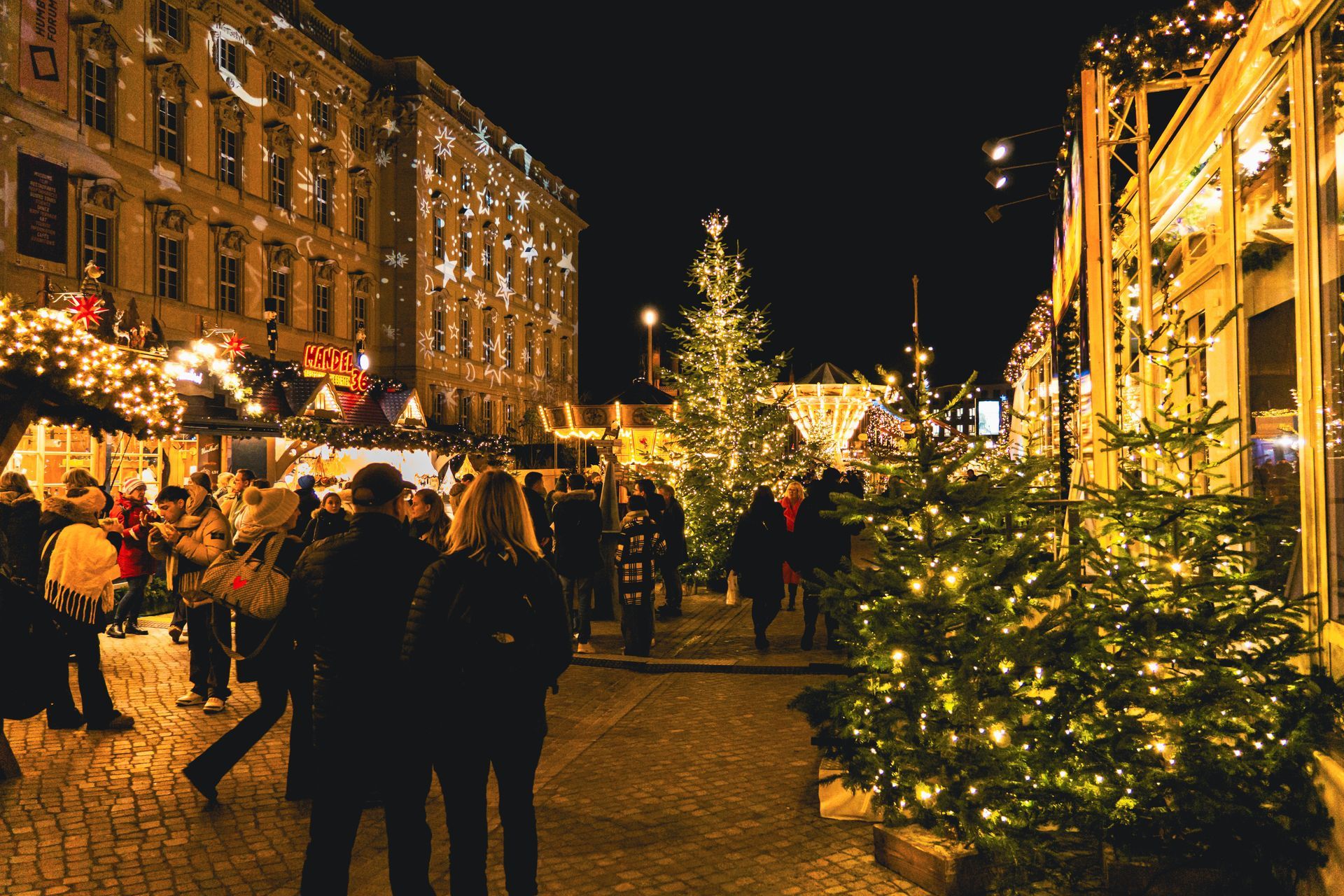 Festive night market with Christmas trees, warm lights, and people walking between stalls