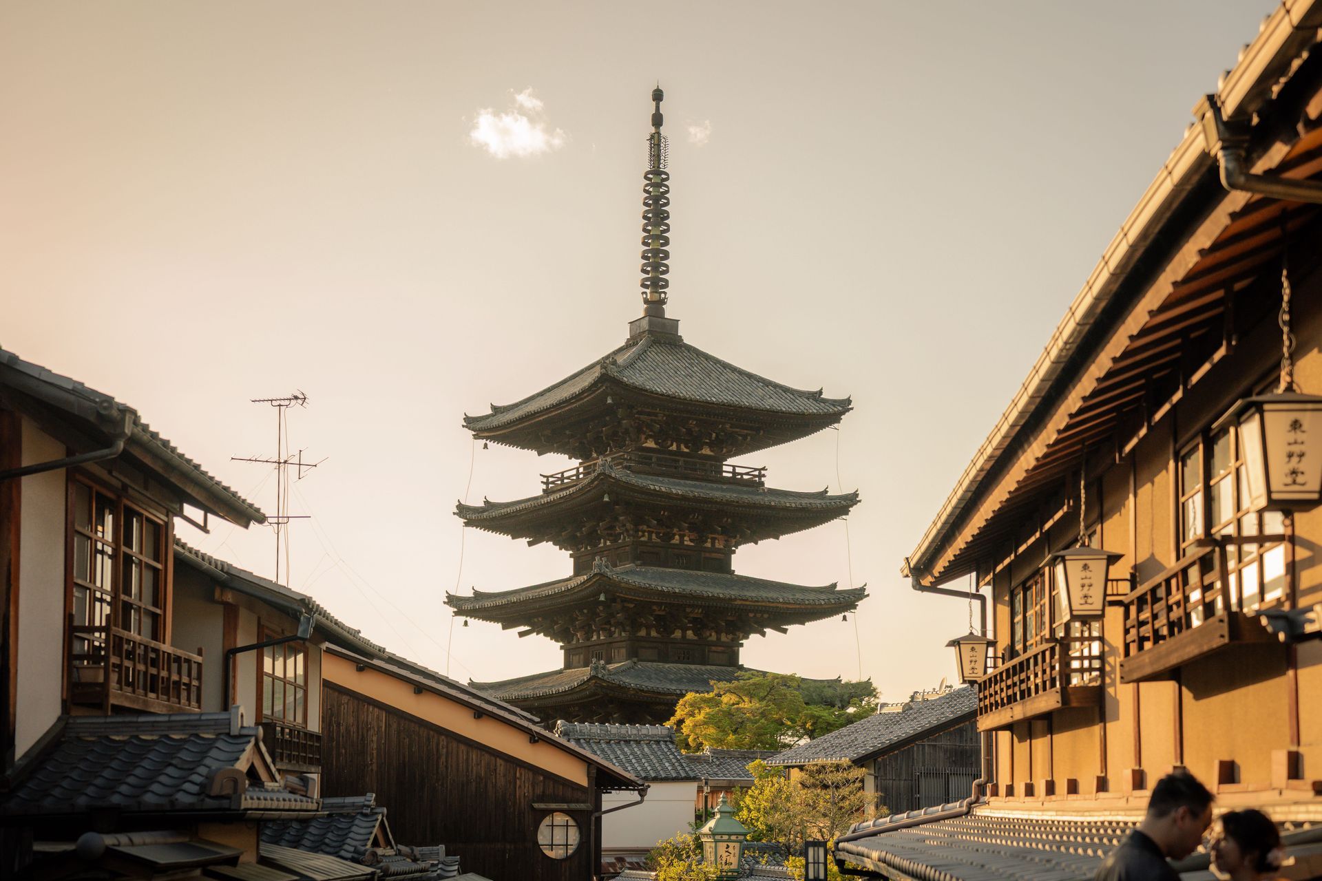 Traditional Japanese pagoda between wooden buildings at sunset, with a clear sky and narrow street
