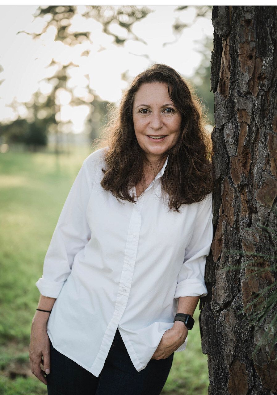 Realtor Liz May leaning against a tree with horse farm in the background