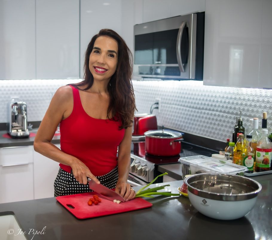 A woman in a red tank top is cutting vegetables on a cutting board in a kitchen.