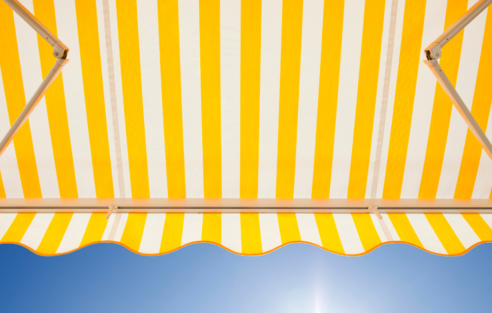 Un store rayé jaune et blanc se détache sur un ciel bleu.