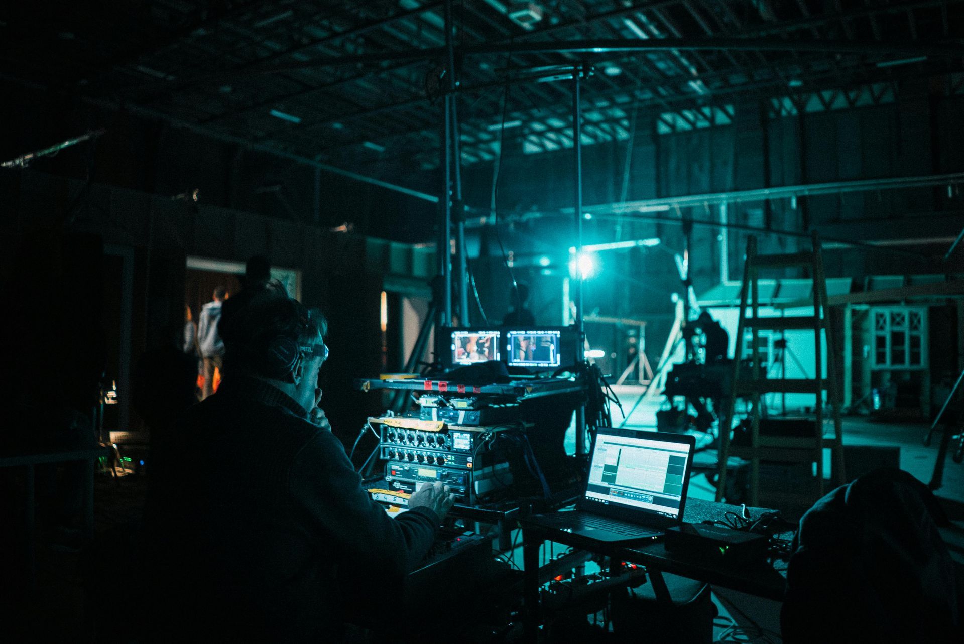 A person operates equipment in a dark room with screens, possibly on a film set.