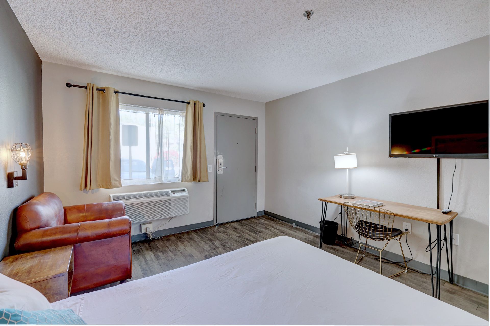 A hotel room with a bed , chair , desk and television.