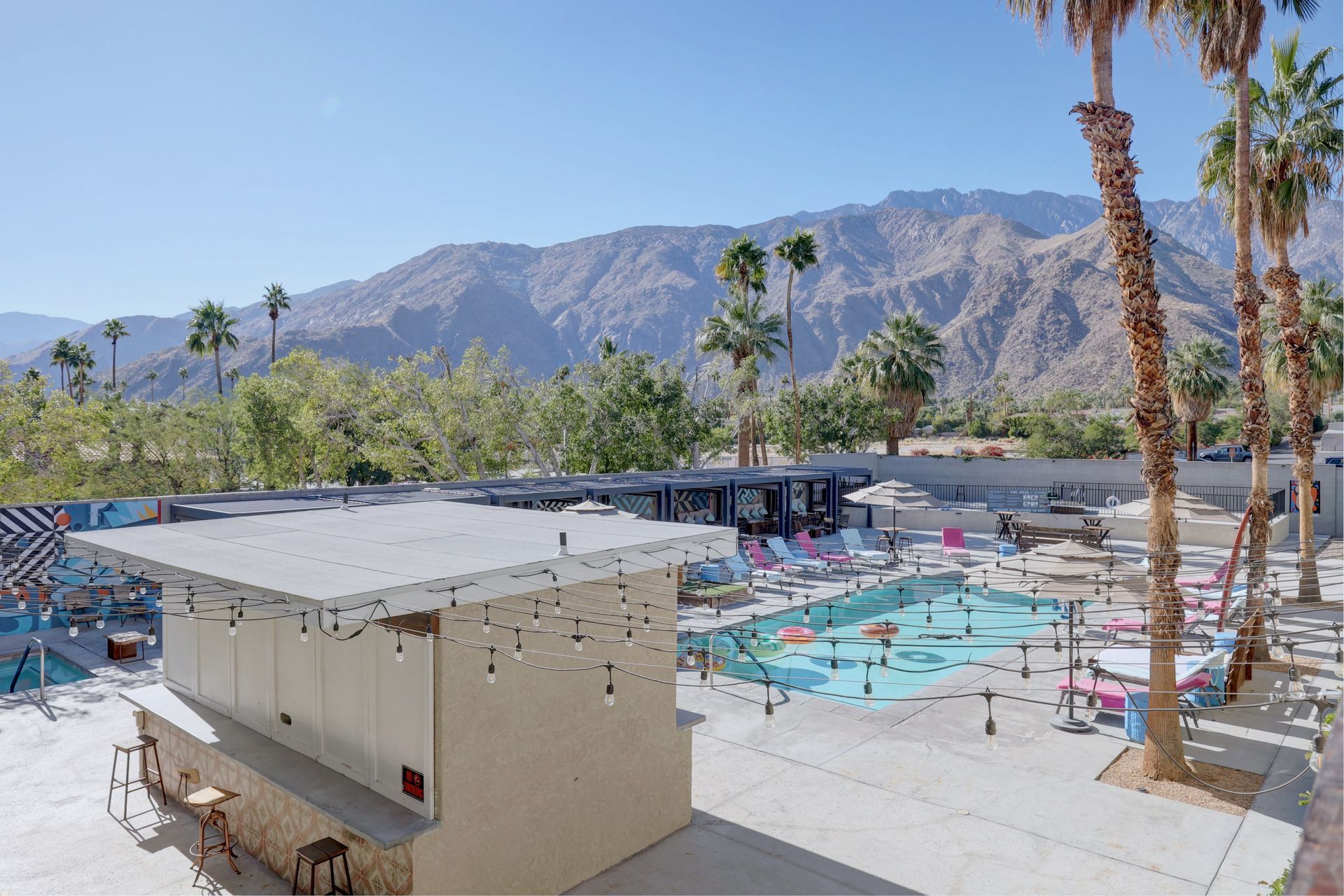 An aerial view of a swimming pool with palm trees and mountains in the background.