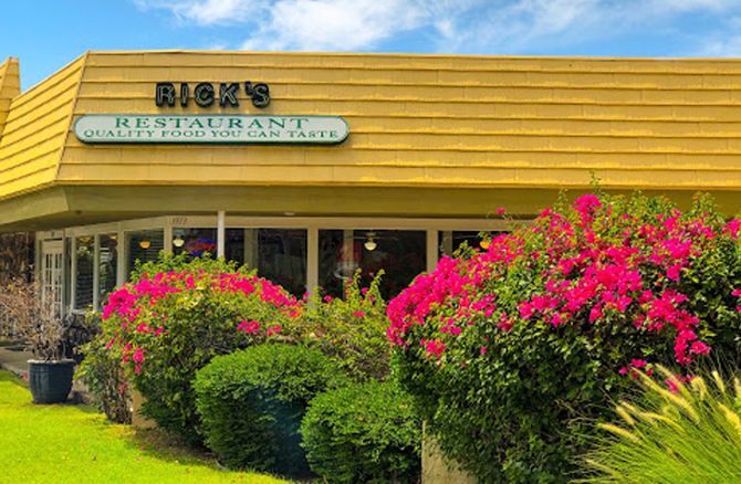 Rick 's restaurant is surrounded by pink flowers and bushes.
