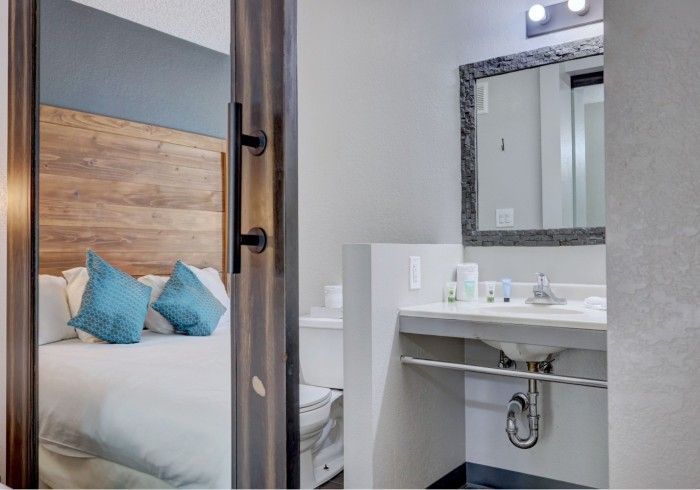 A hotel room with a bed and a bathroom with a sink and mirror.